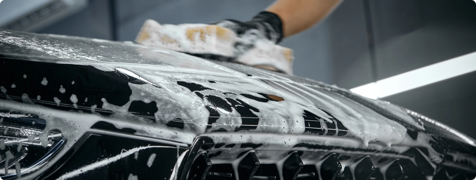 Handmatige reiniging van het exterieur van een auto met snowfoam tijdens een professionele detailingbehandeling.